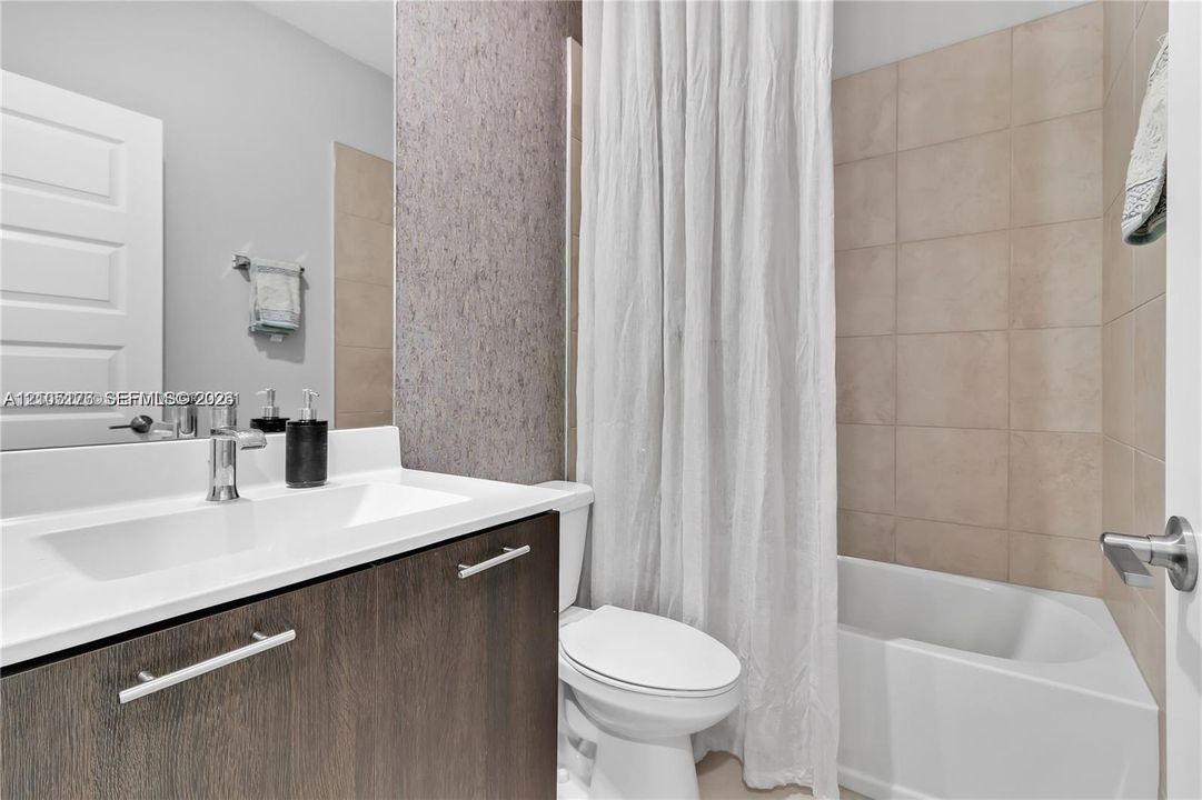 Bathroom featuring a dark wood-finish vanity with a white countertop, integrated rectangular sink, chrome fixtures, and a tub with neutral tile surround