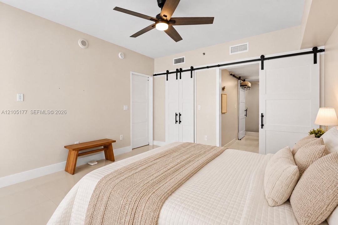 Neutral wall palette featuring white barn-style sliding doors with matte black hardware, recessed ceiling lighting, and a dark-finish ceiling fan