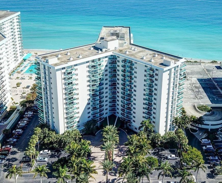 High-rise residential structure featuring tiered balconies, a paved circular entryway, and extensive tropical landscaping