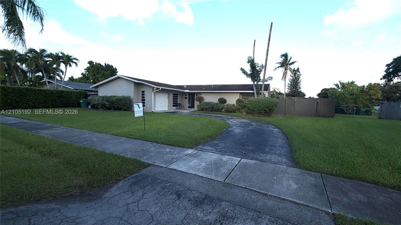 Single-story residence featuring a concrete exterior, attached garage, curved driveway, and established landscaping