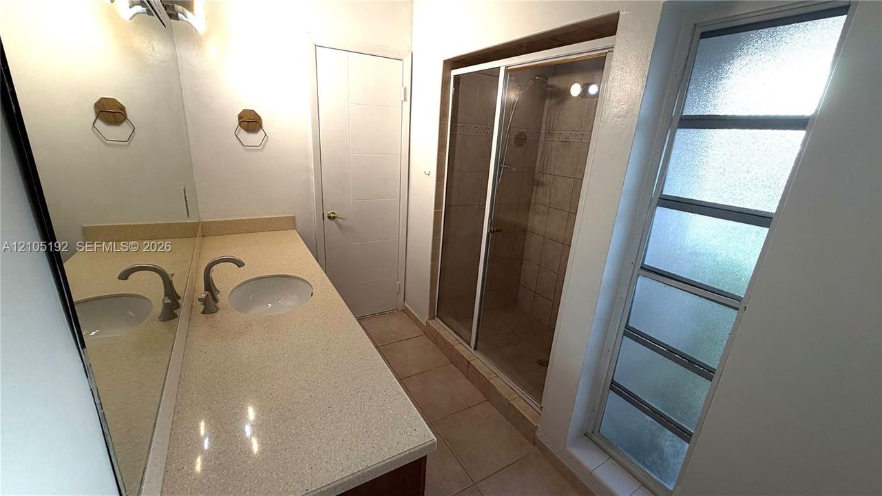 Dual vanity with undermount sinks and light-toned countertop, framed mirror, tiled shower with sliding glass door, and privacy windows