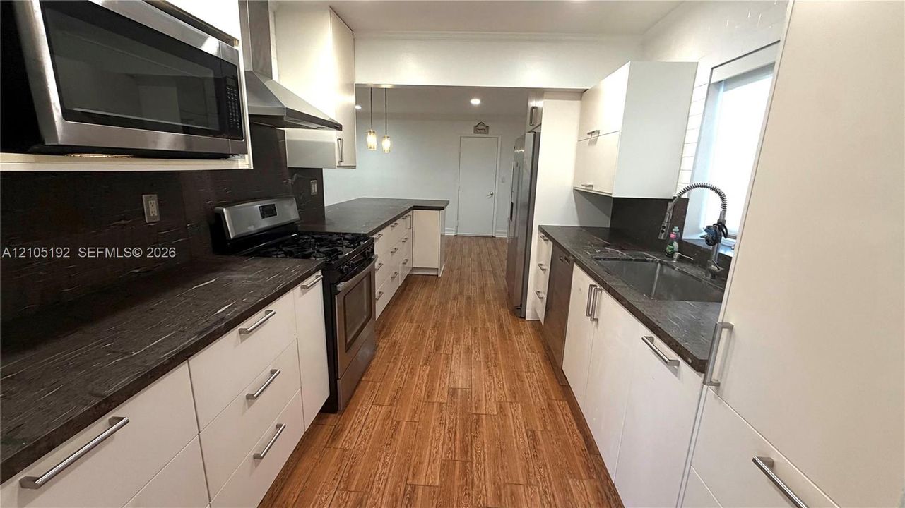 Contemporary kitchen featuring white cabinetry, dark countertops, stainless steel appliances, and wood-finish flooring