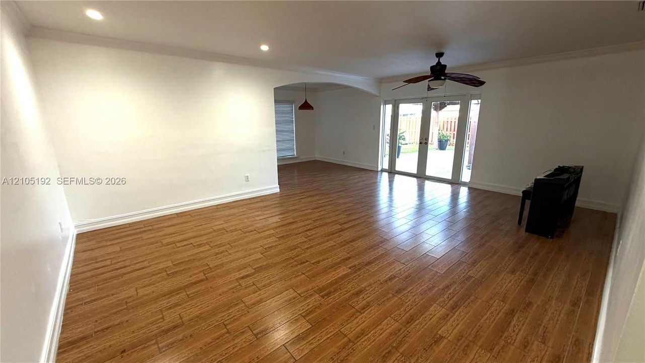 Wide plank wood-finish flooring, recessed lighting, crown molding, double French doors, and an arched doorway