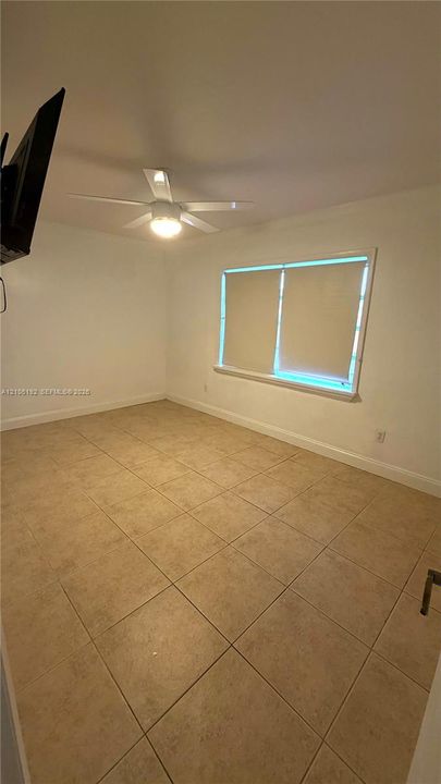 Neutral-toned tile flooring, ceiling fan with integrated lighting, and a window with blinds