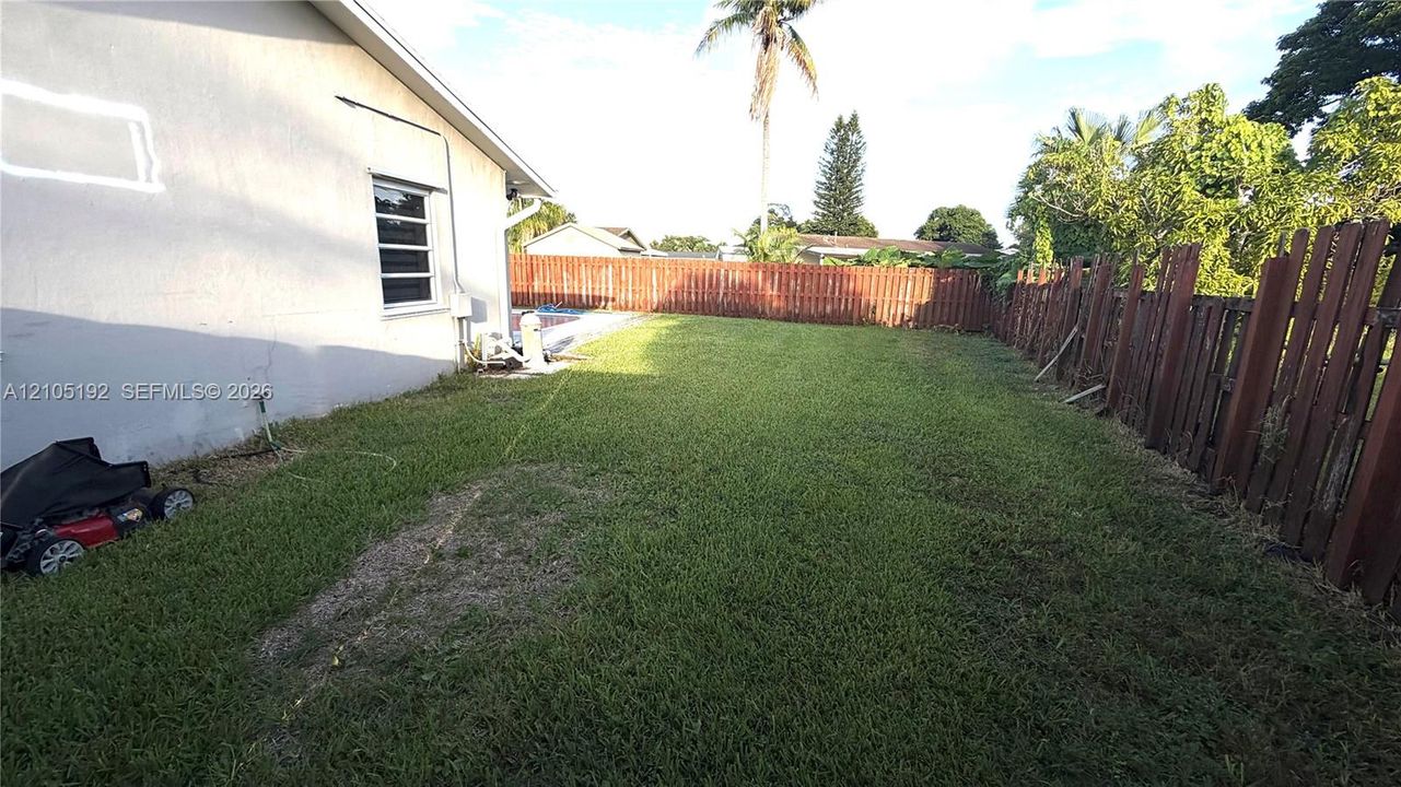 Enclosed backyard featuring a brown wooden fence, expansive lawn, and concrete patio area