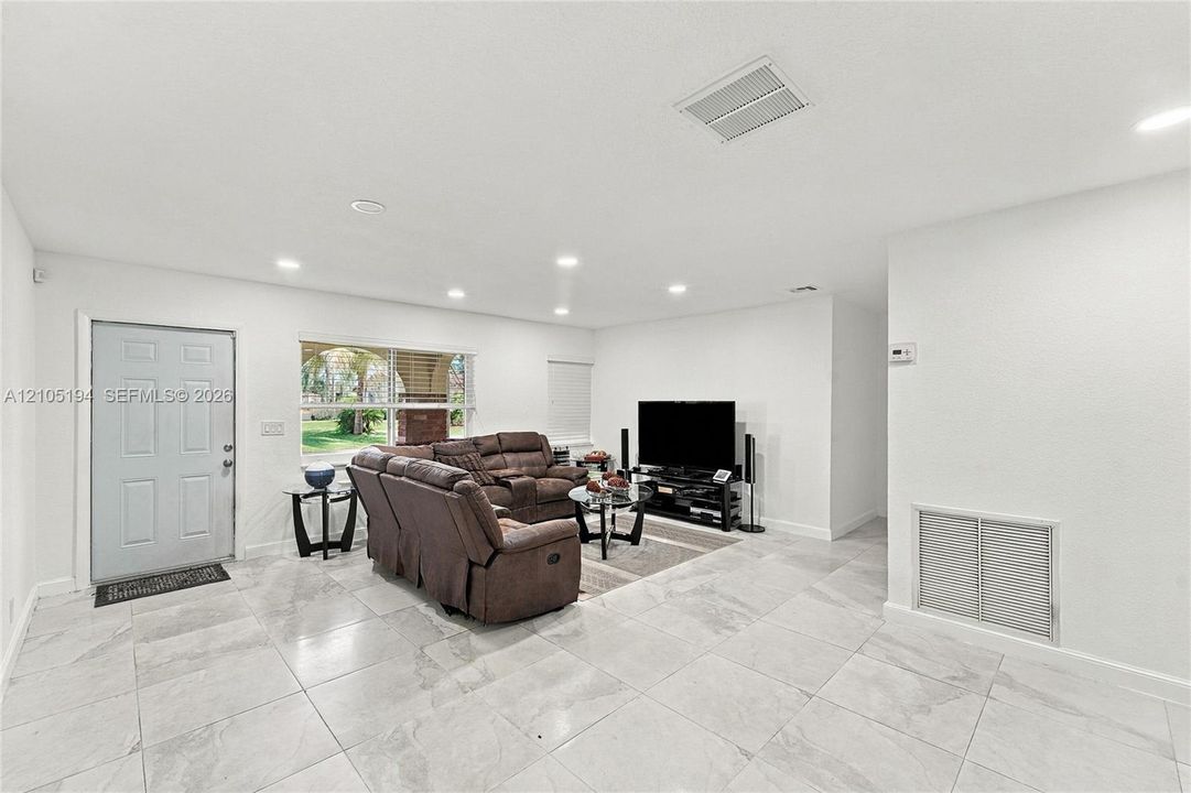Living area featuring large-format ceramic tile flooring, recessed ceiling lighting, and a multi-panel exterior door