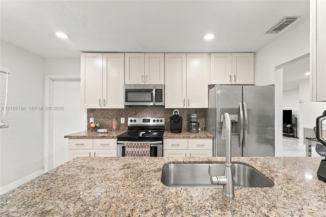 Kitchen featuring light-toned cabinetry, expansive stone-finish countertops, stainless steel appliances, and a double-basin undermount sink with a gooseneck faucet