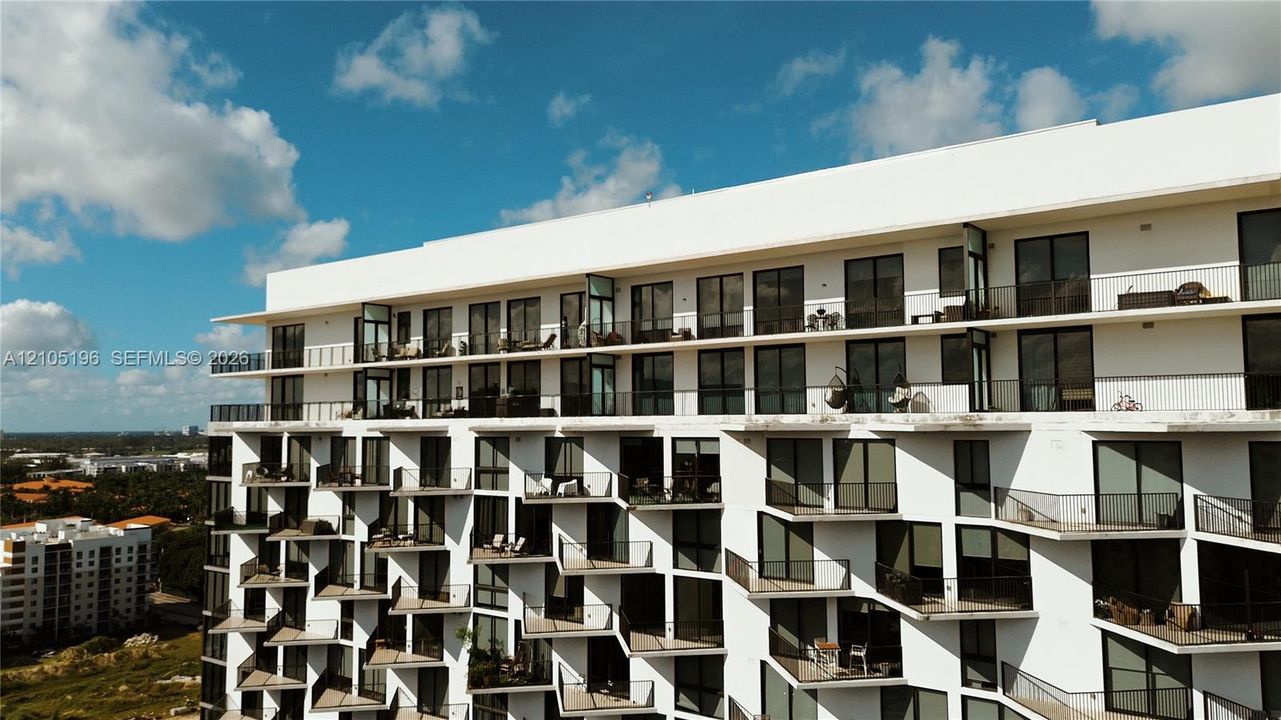 Modern high-rise residential building with white exterior, multiple private balconies, and large windows