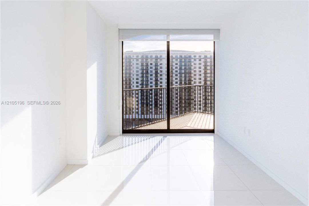 Sliding glass door leading to an exterior balcony with metal railings, featuring white tile flooring and pristine white walls