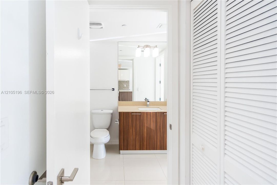 Bathroom featuring a wood-finish vanity with a light-toned countertop, a rectangular mirror, a three-light vanity fixture, and white louvered bifold doors
