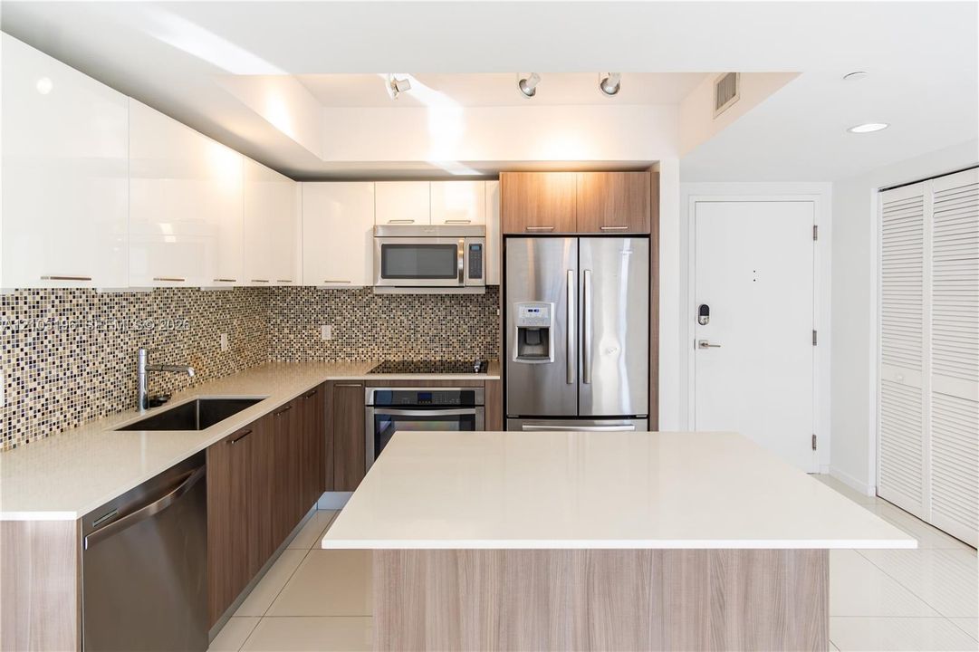 Modern kitchen featuring wood-finish cabinetry, white countertops, mosaic tile backsplash, and stainless steel appliances