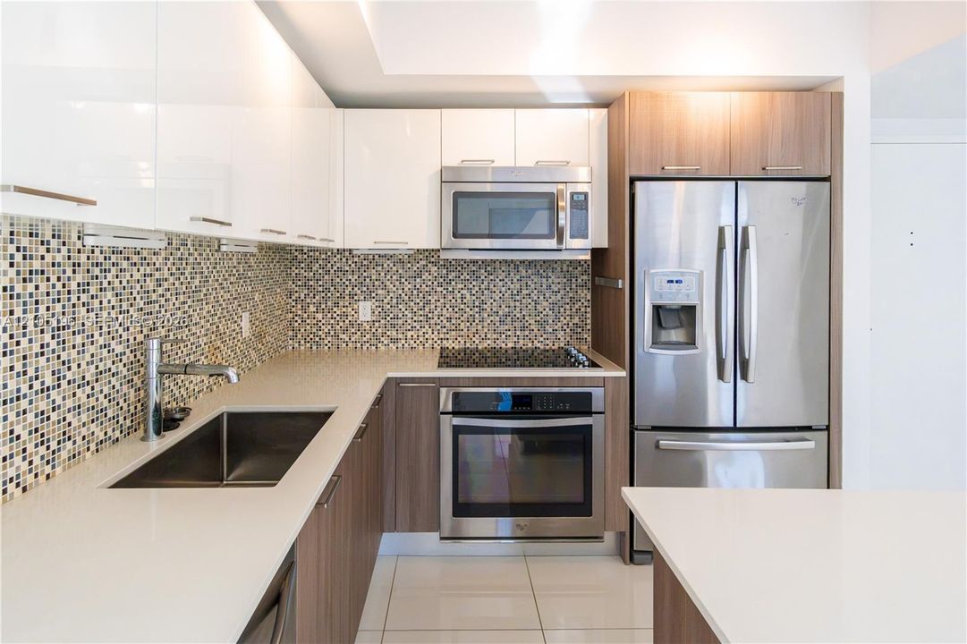 Modern kitchen featuring white upper cabinetry, wood-finish lower cabinetry, a mosaic tile backsplash, stainless steel appliances, and solid surface countertops