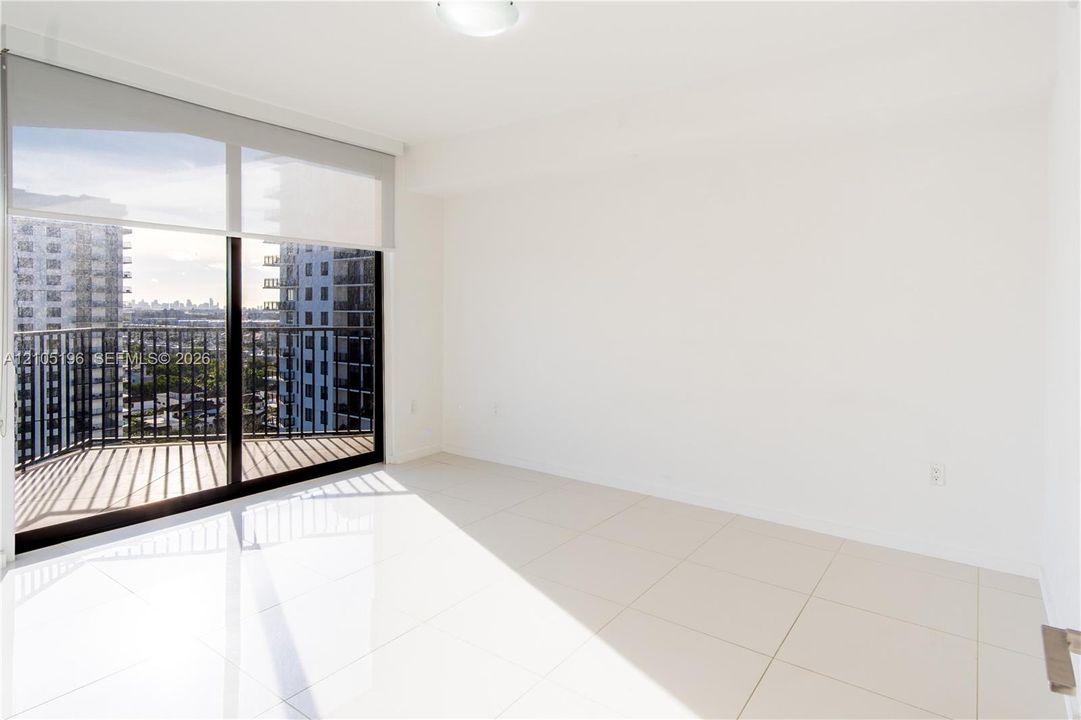 Expansive sliding glass doors, balcony access, white tile flooring, ceiling-mounted light fixture, and neutral wall tones