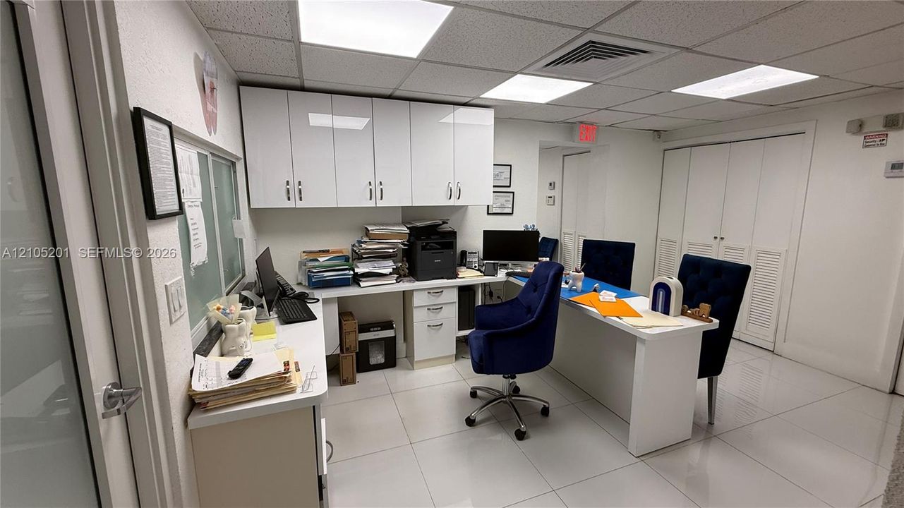 Recessed ceiling with integrated lighting, white wall-mounted cabinetry, built-in desk with integrated storage, white tile flooring, and louvered closet doors