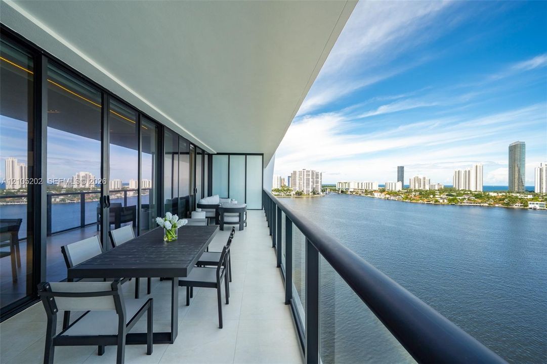 Expansive covered balcony featuring large-format tile flooring, a sleek metal railing, and extensive floor-to-ceiling glass sliding doors
