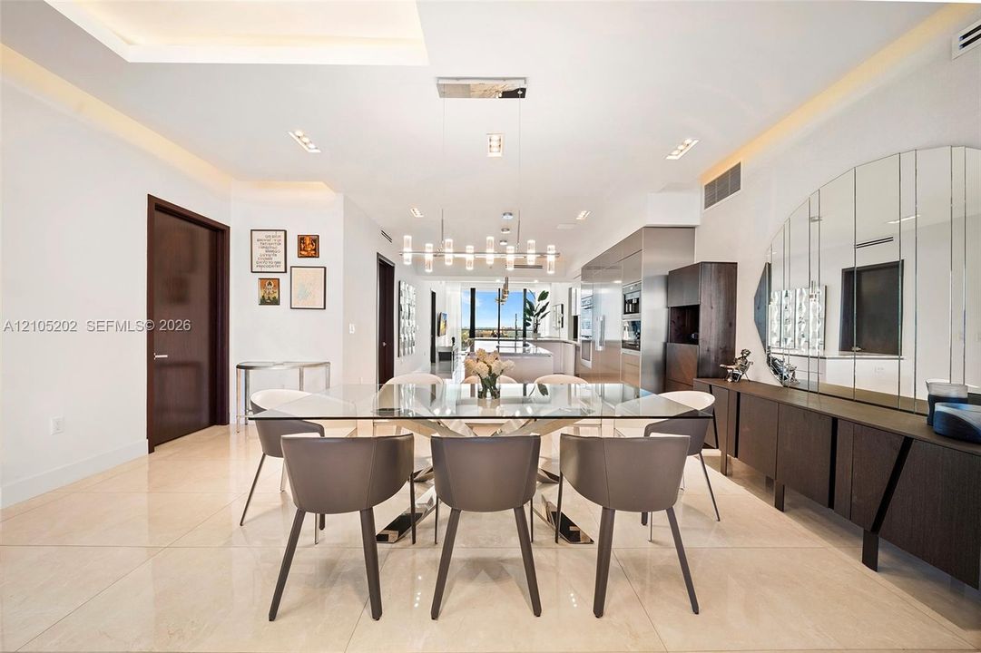 Open-concept dining and kitchen area showcasing polished light-tone flooring, modern pendant lighting, and a spacious island with seating