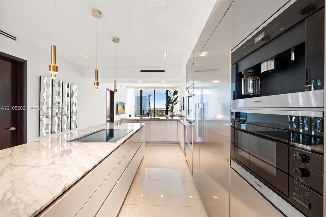 Sleek kitchen featuring a central island with a stone countertop, high-gloss flat-panel cabinetry, integrated Miele wall appliances, and cylindrical pendant lighting