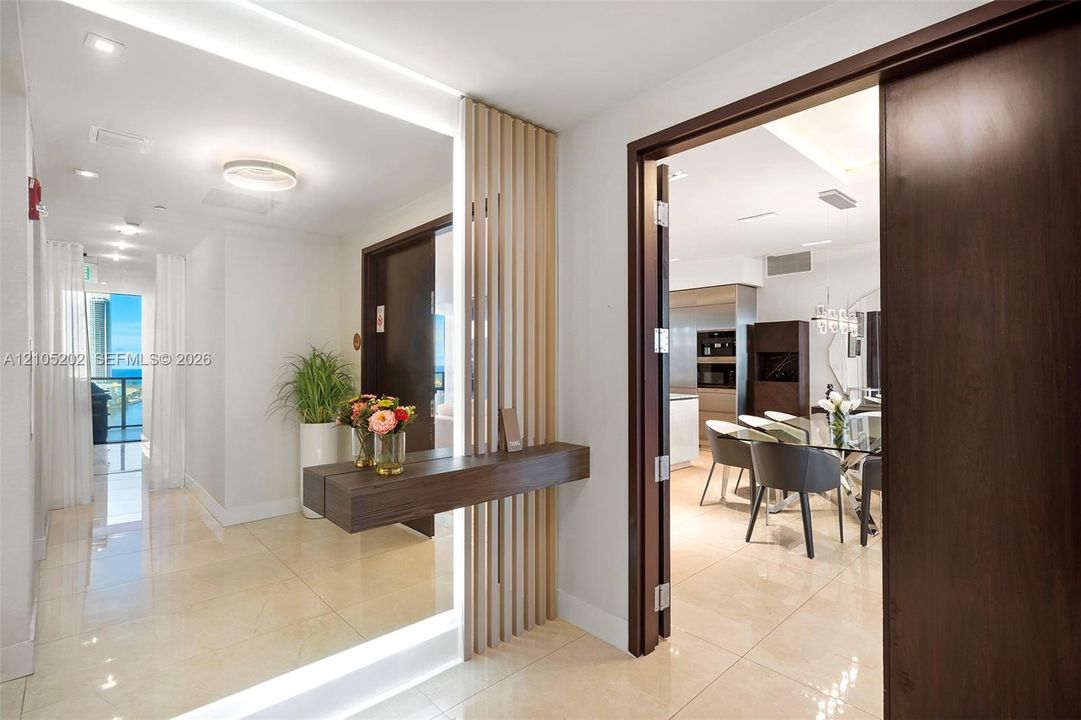 Entryway featuring large-format tile flooring, a floor-to-ceiling mirror with integrated lighting, a light-finish wood slat privacy screen, and a cantilevered wood-finish console shelf