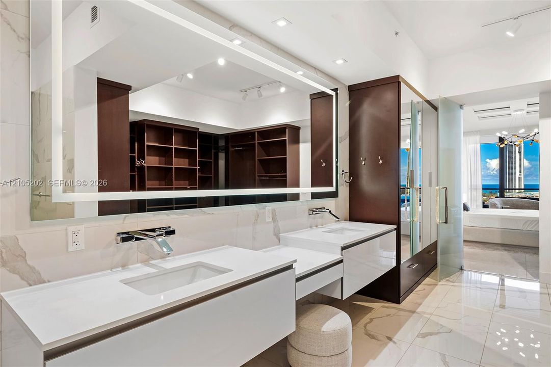 Floating dual-vanity featuring white countertops, integrated rectangular sinks, wall-mounted chrome faucets, and an oversized illuminated mirror