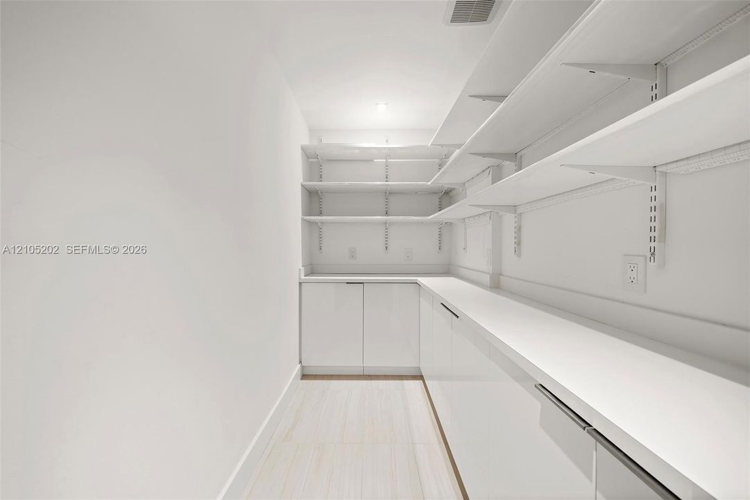 Storage area featuring floor-to-ceiling adjustable shelving, extensive solid-surface countertops, high-gloss cabinetry, and light-toned flooring