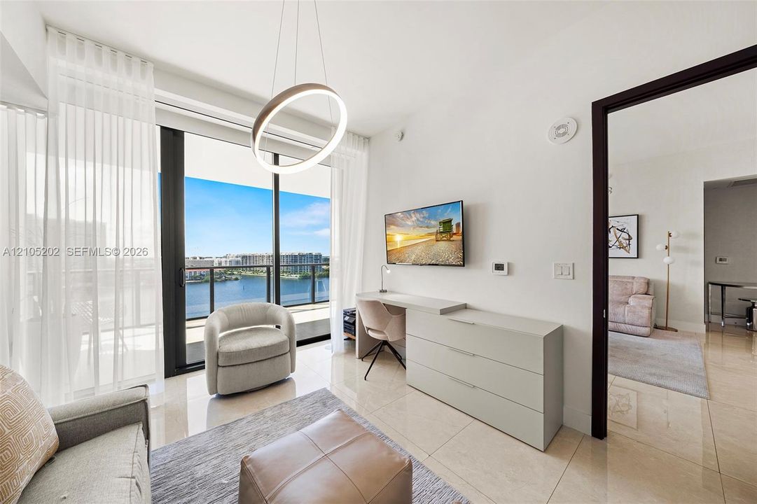 Floor-to-ceiling sliding glass doors, polished tile flooring, circular pendant lighting, and a private balcony overlooking the water