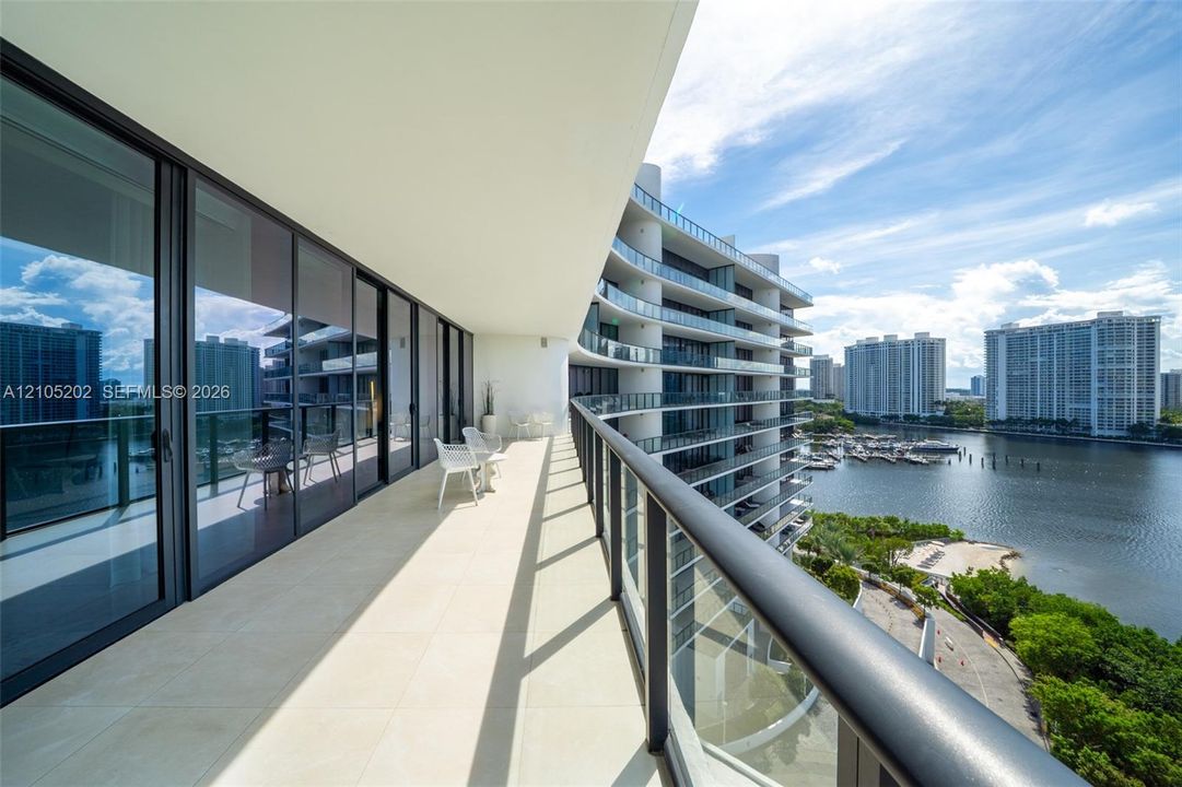 Expansive covered balcony featuring large-format tile flooring, a sleek metal and glass railing system, and floor-to-ceiling sliding glass doors