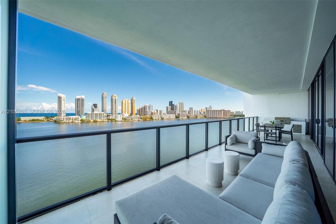 Expansive balcony featuring neutral tile flooring, glass-paneled railing, and built-in outdoor kitchen cabinetry