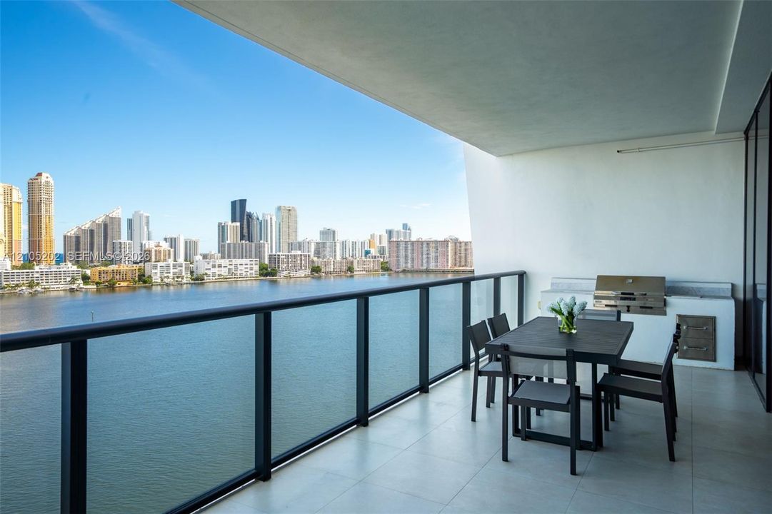 Covered balcony featuring tile flooring, glass-paneled railing, and built-in stainless steel outdoor kitchen components