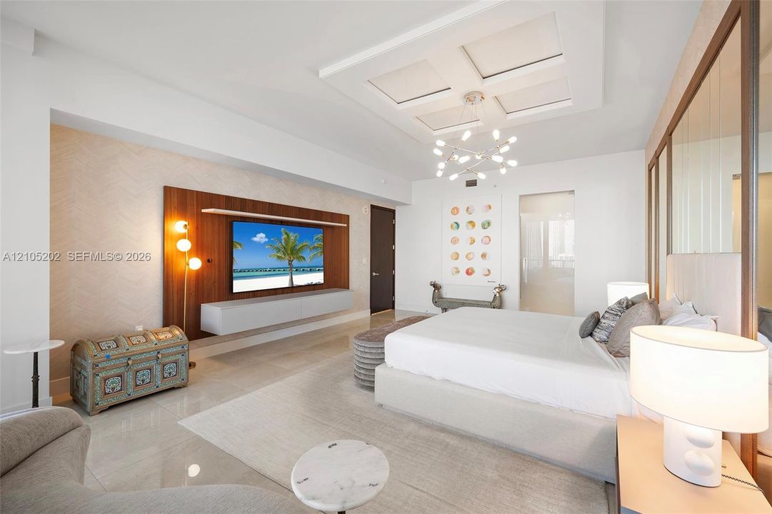 Coffered ceiling with modern multi-arm chandelier, wall-mounted wood-panel media feature, floating cabinetry, and tile flooring