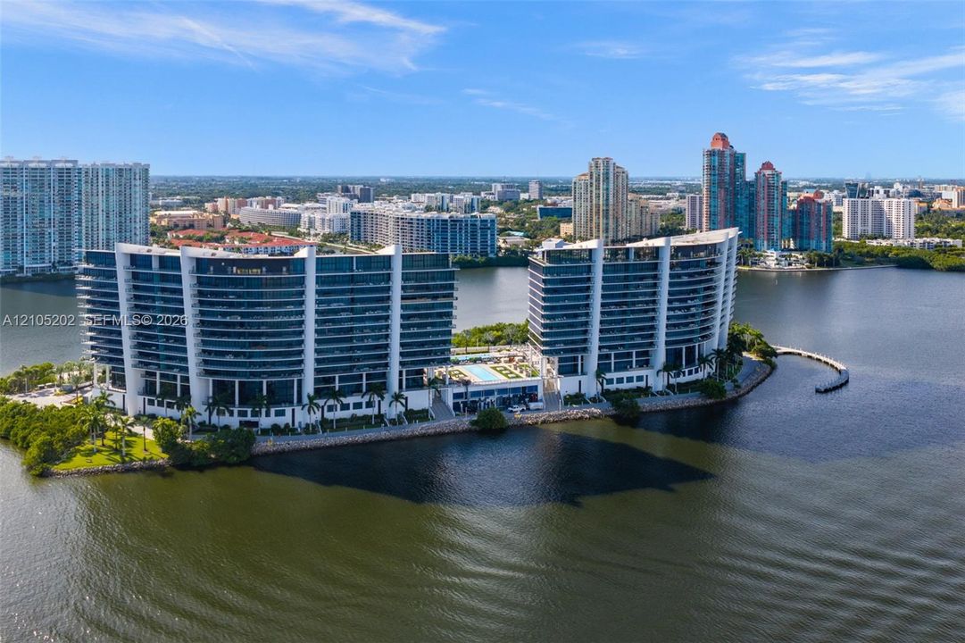 Waterfront high-rise complex featuring private balconies, a ground-level swimming pool, and extensive shoreline landscaping