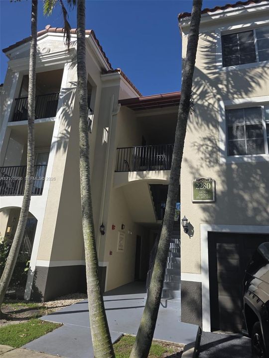 Stucco exterior featuring multi-level balconies with black metal railings, tile roof accents, and attached garage
