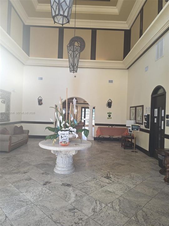 Grand foyer featuring double-height tray ceilings, stone tile flooring, arched architectural detailing, and dual pendant light fixtures