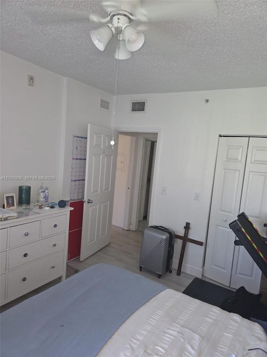 Neutral interior room featuring wood-finish flooring, a ceiling-mounted light fixture with a fan, and white paneled closet doors