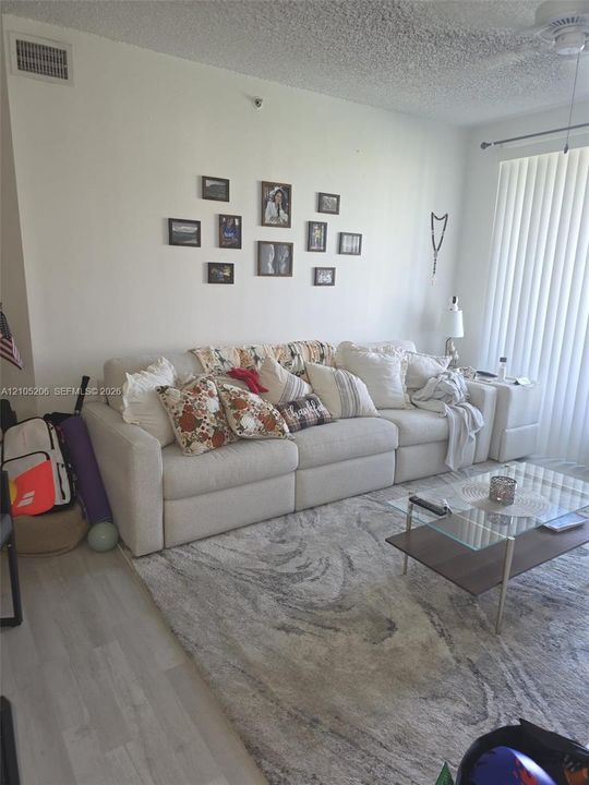 Living area featuring wood-finish flooring, textured ceiling, and floor-to-ceiling vertical blinds