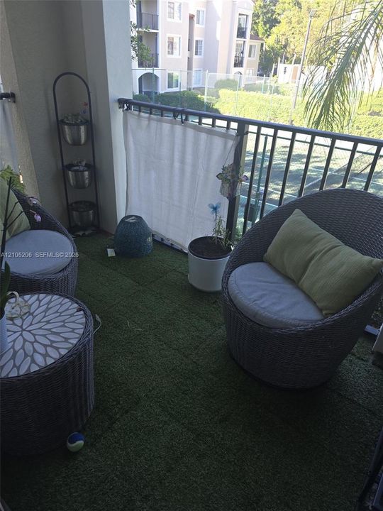 Covered balcony featuring synthetic grass flooring, metal railings, and a concrete ceiling
