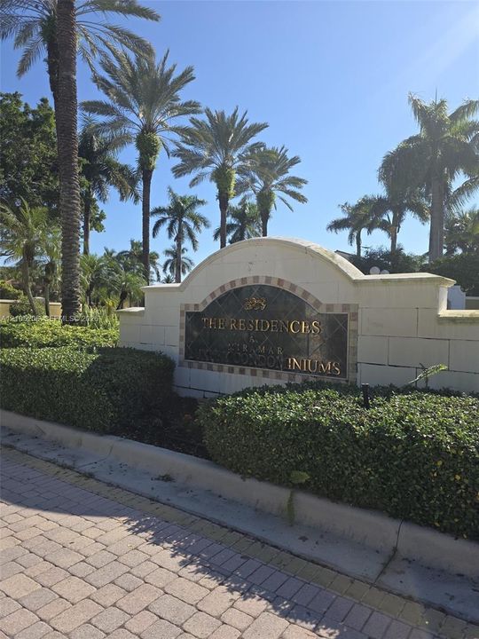 Stone-clad monument signage featuring metal lettering, surrounded by manicured shrubbery and mature palm trees with stone paver entryway