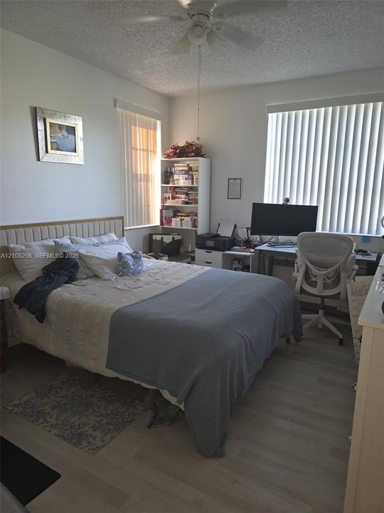 Room featuring wood-finish flooring, textured ceiling, central ceiling fan with integrated lighting, and dual windows with vertical blinds
