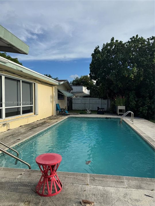 Outdoor swimming pool with tiled coping and deck, integrated entry steps, and a perimeter fence