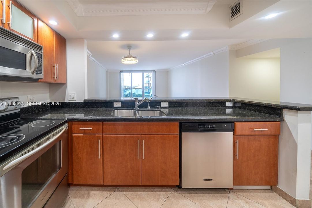 Kitchen featuring wood cabinetry, stone countertops, stainless steel appliances, and tile flooring