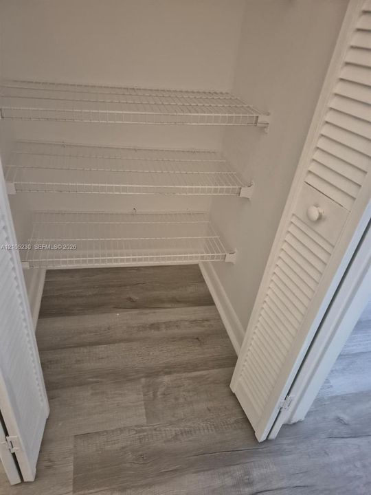 Storage closet featuring louvered bi-fold doors, three tiered wire shelves, and wood-finish flooring