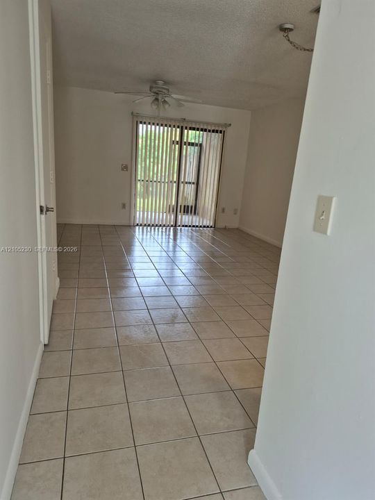 Open interior space featuring light-toned tile flooring, ceiling fan with integrated lighting, and vertical blinds covering the sliding glass doors