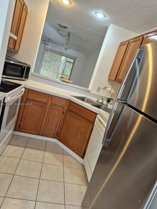 Kitchen featuring natural wood cabinetry, stainless steel refrigerator, white appliance suite, tile flooring, and recessed lighting
