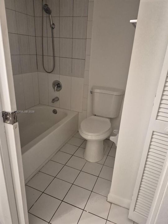 Bathroom featuring a tub-shower combination, vertical tile shower surround, square floor tiling, and a standard-height toilet
