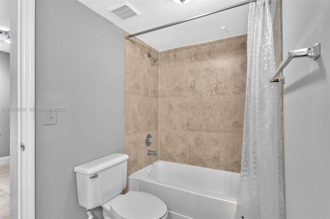 Bathtub with a tiled surround, chrome shower fixtures, and a white toilet