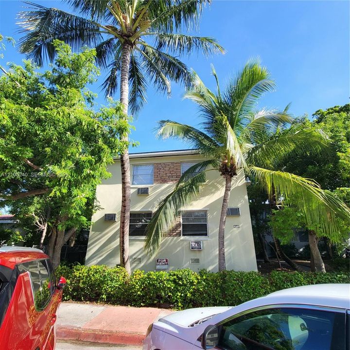 Two-story exterior with a brick accent facade, multiple windows, and mature palm trees
