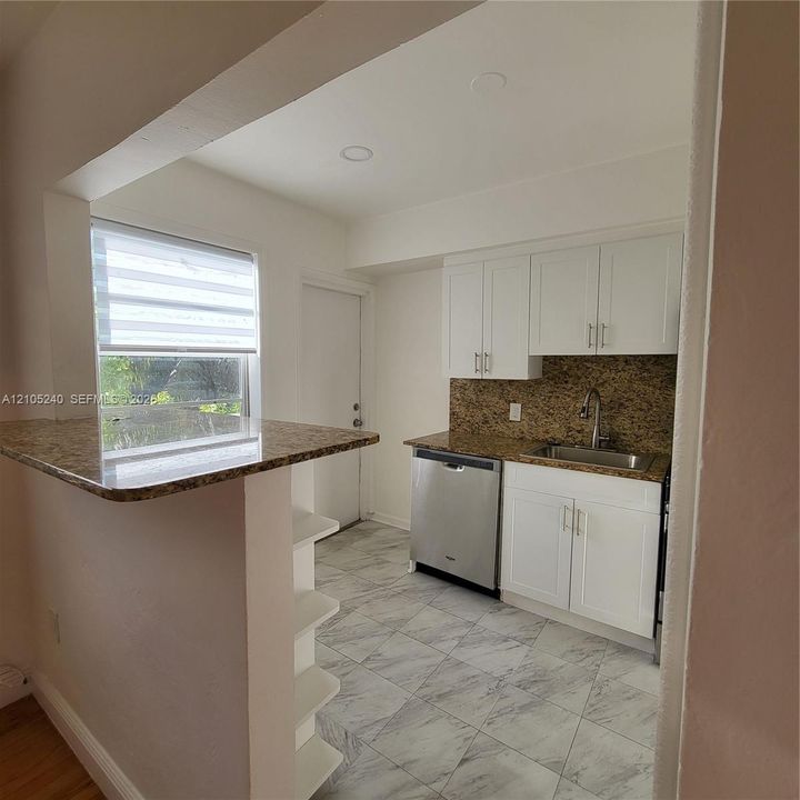 Kitchen featuring white shaker cabinetry, granite countertops, tile backsplash, stainless steel dishwasher, and a built-in breakfast bar with shelving