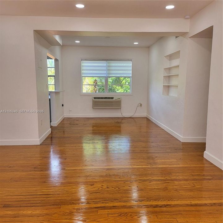 Hardwood flooring, recessed lighting, built-in shelving, window with blinds, and a wall-mounted air conditioning unit