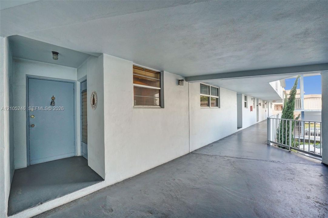 Exterior walkway featuring smooth stucco walls, solid-core entrance door, recessed overhead lighting, and white metal railings