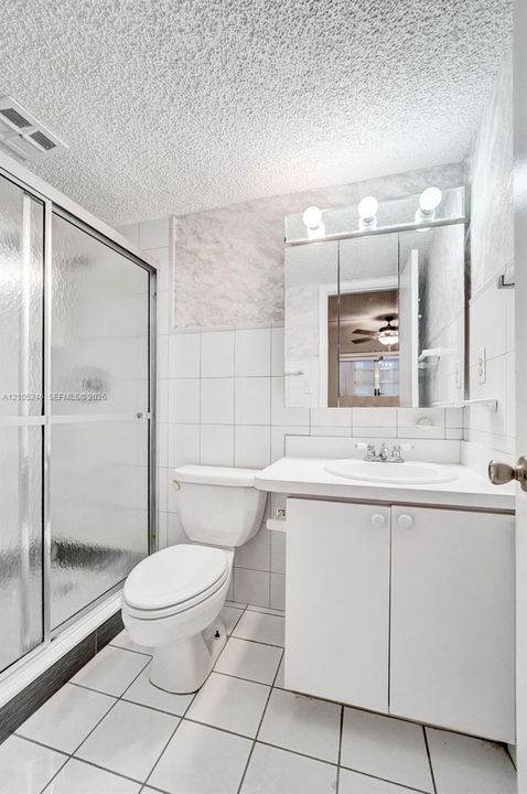 Bathroom featuring a walk-in shower with metal-framed glass doors, white tiled walls, a vanity with a white countertop and integrated sink, and a triple-light fixture above a mirrored cabinet