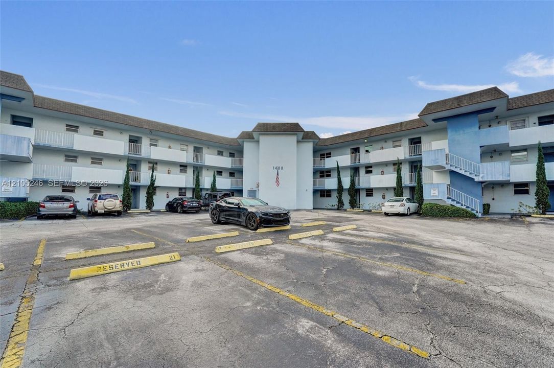 Multi-story apartment building exterior featuring paved surface parking, covered exterior corridors, and vertical landscaping accents
